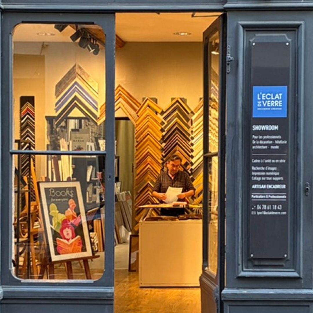 A view into a framing shop with a person working and numerous frame samples on the walls.