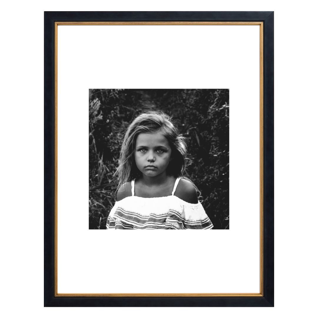 Black and white portrait of a young girl with a serious face and ruffled top, framed.