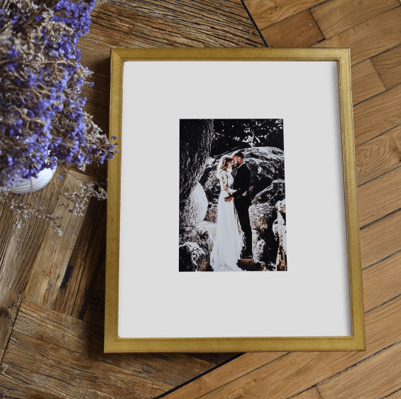 Gold framed black and white wedding photo of a couple embracing, next to dried flowers.