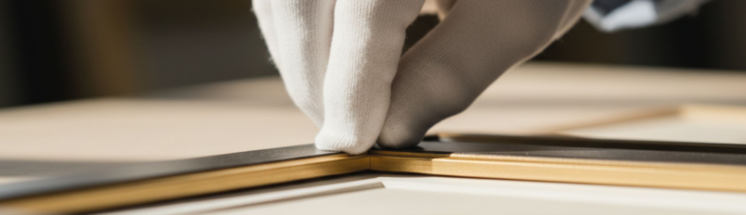 Gloved hands carefully align a section of an intricate golden picture frame.