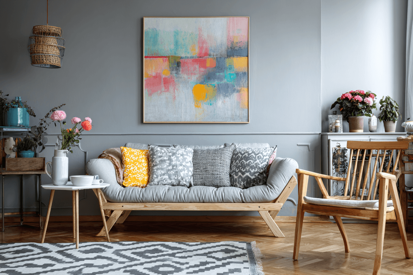A modern living room with a gray sofa, abstract painting, wooden chair, and colorful pillows.