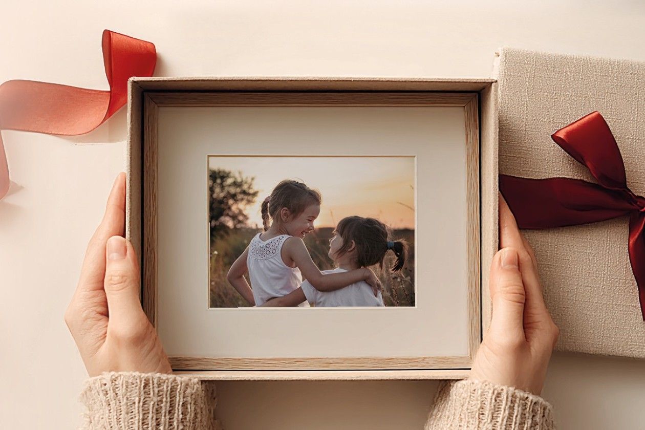 Hands hold an open gift box revealing a framed photo of two girls hugging.