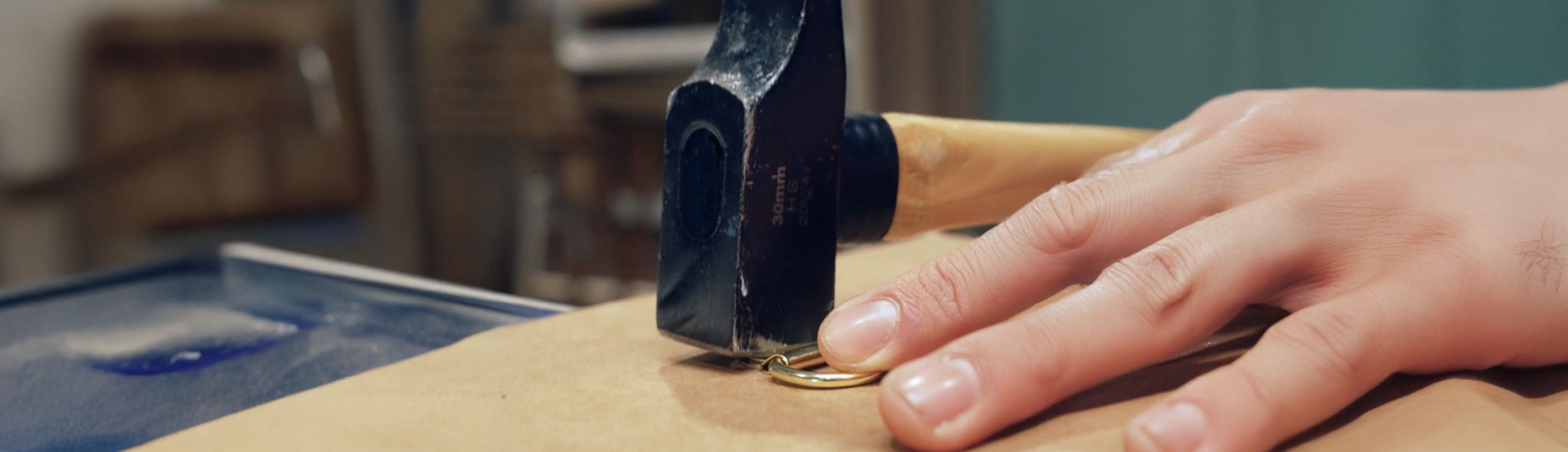 A person's hand holds a hammer striking a light-colored surface.