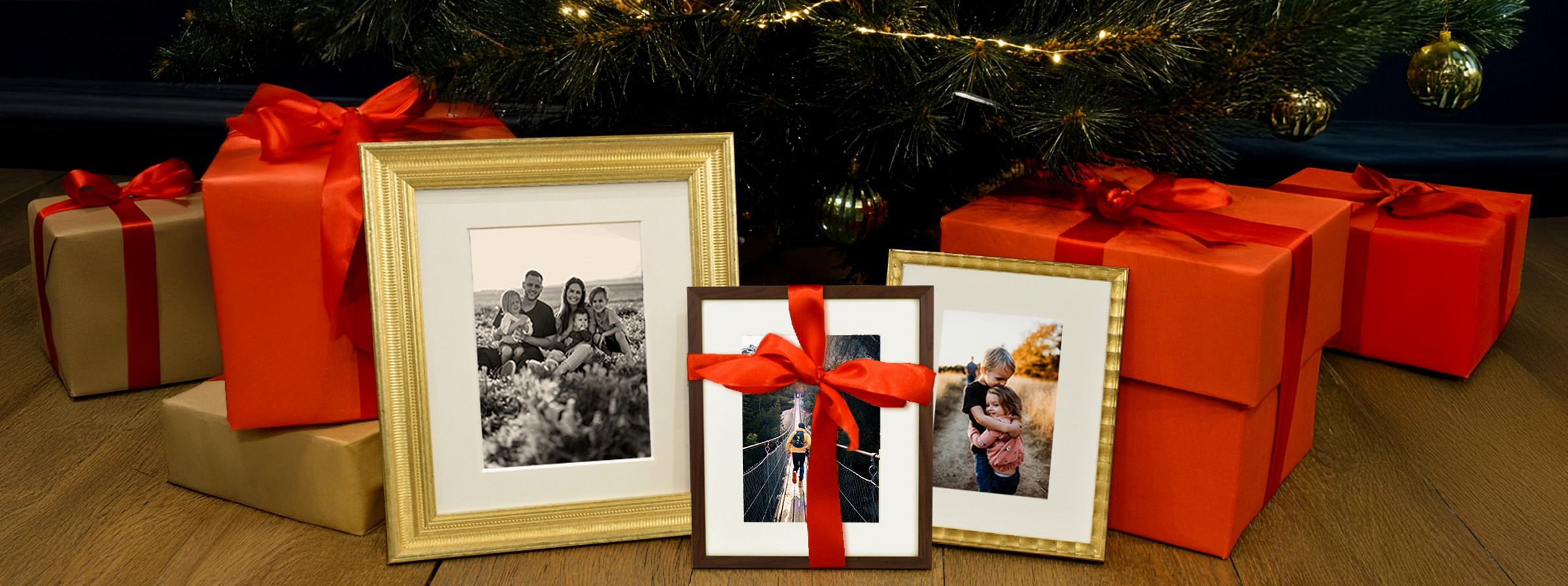 Framed photos and red wrapped gifts are arranged under a festive Christmas tree.