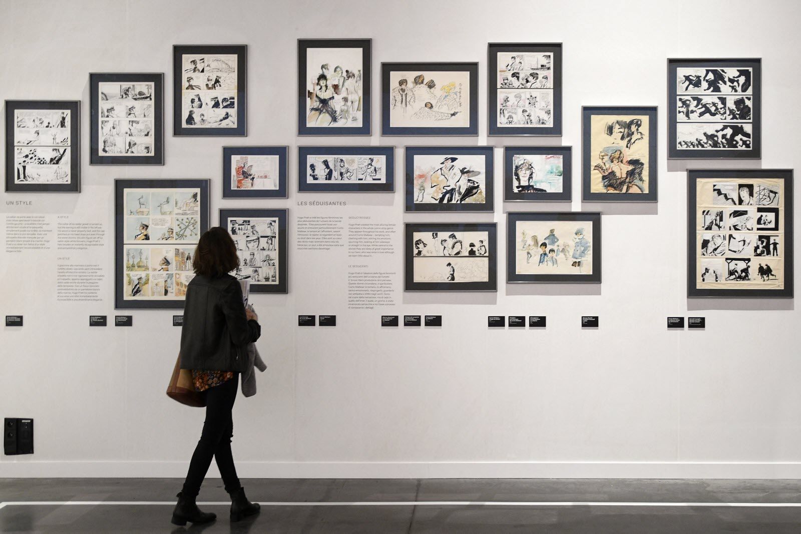 Person views a gallery wall filled with numerous framed comic strip and manga artworks.